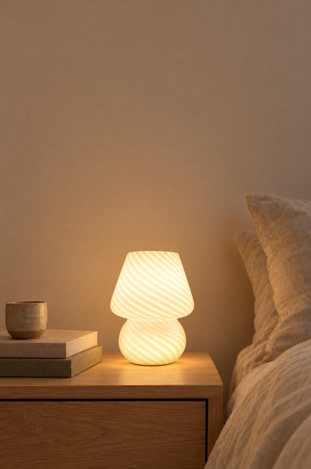 Weiße Pilzlampe aus gestreiftem Glas leuchtet warm auf einem Nachttisch aus Holz